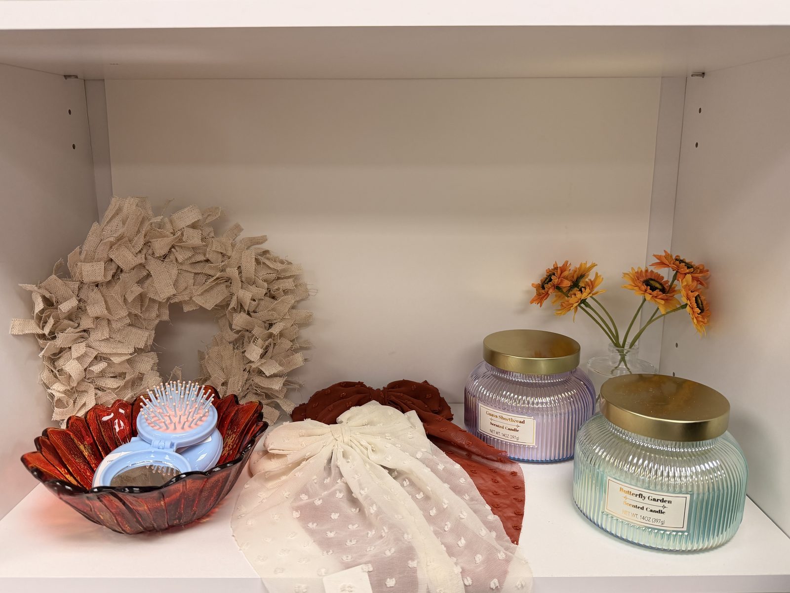A burlap wreath, scented candles, and a sunflower vase styled on a Soco Chic shelf
